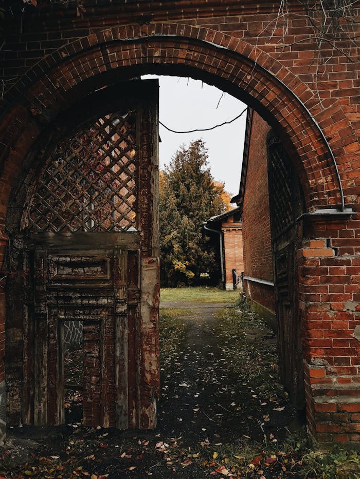 Prestations An abandoned brick archway leading to a rustic courtyard, surrounded by autumn foliage.