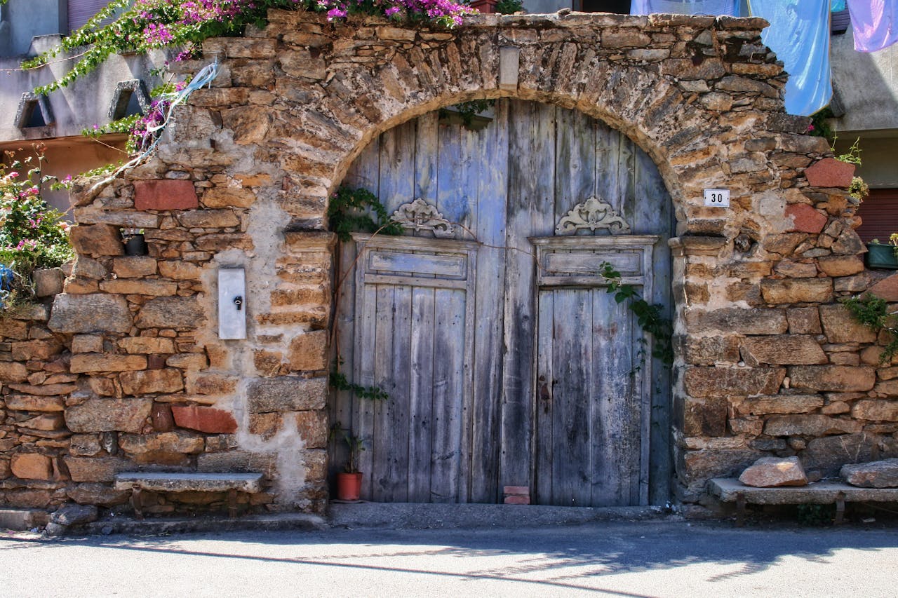 Prestations Historic stone archway with wooden doors in sunny Sardinia, Italy.